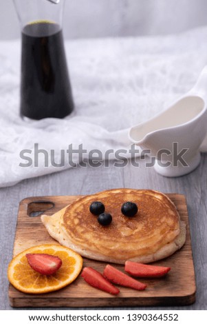 Homemade pancakes with berries and honey on a pink plate over white wooden surface
