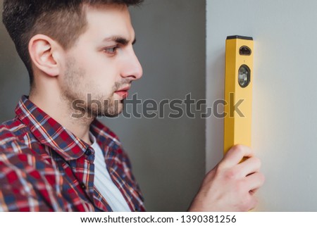 Picture of a young confident  man is holding a ruler, a belt hanging tools and measure the wall!