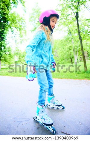 Cute little child girl learning to roller skate on beautiful summer day in a park. Child wearing safety helmet enjoying roller skating ride outdoors