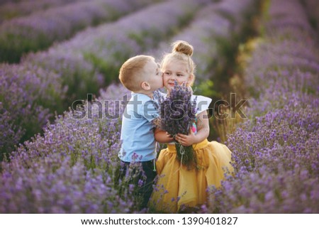 Playful little cute couple boy girl walk on purple lavender flower meadow field background, have fun, kiss, enjoy good sunny day. Excited small kids. Family day, children, childhood lifestyle concept