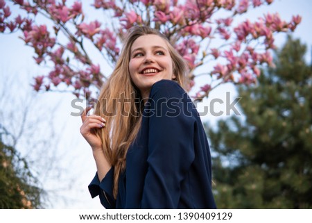 Portrait of Beautiful blonde girl posing with blooming Magnolia tree branches with pink flowers on background. Spring season