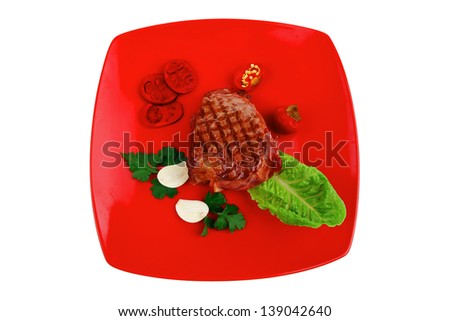 meat savory : beef grilled and garnished with green lettuce and red chili hot pepper on red plate isolated over white background