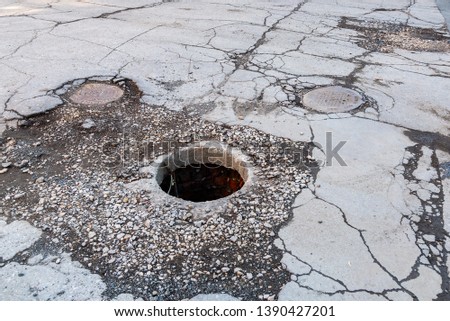 Open unsecured sewer manhole on the asphalt road. Dangerous pit on the road. Old sewer well hatch on the street