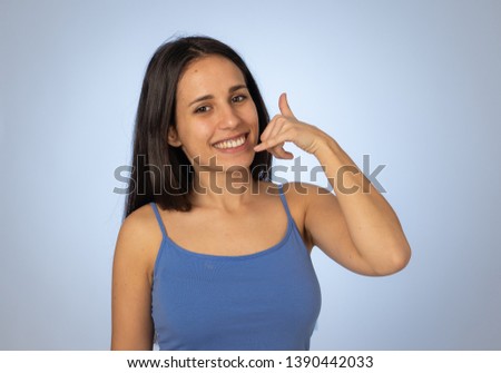 Give me a call. Close up portrait of beautiful latin woman making call you gesture smiling. Young hispanic female with hand shaped like phone isolated on blue background. Image friendly advertising.