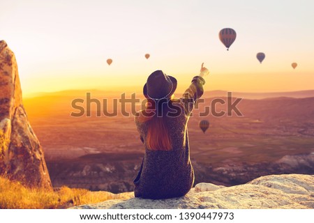 A woman alone unplugged sits on top of a mountain and admires the flight of hot air balloons in Cappadocia in Turkey. Digital detox and soul search Royalty-Free Stock Photo #1390447973