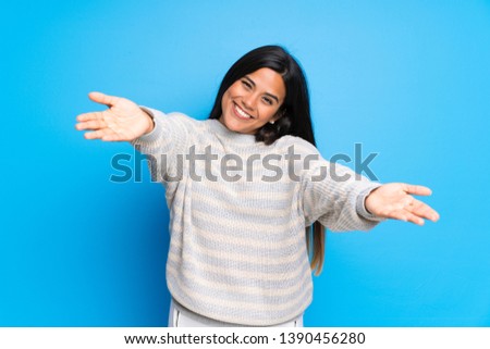 Young Colombian girl with sweater presenting and inviting to come with hand