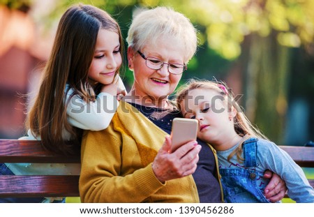 Happy family. Grandmother sitting in the park with granddaughters and having fun with smartphone. Lifestyle concept