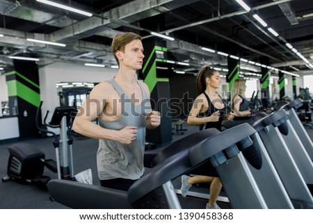 Picture of people running on treadmill in gym. Handsome trainer and two young women on the treadmill in gym. Fitness concept