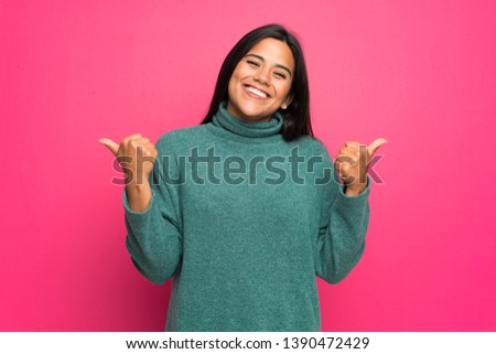 Young Colombian girl with green sweater with thumbs up gesture and smiling