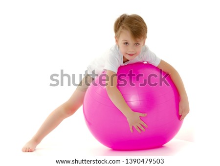 Cute little boy on the big ball is engaged in fitness. On it is a pure white T-shirt on which you can make a picture or write text. The concept of sports, advertising. Isolated on white background.