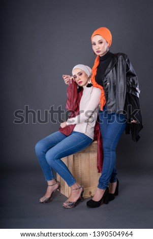 Fashionable female models in jeans, long sleeves leather jacket and turban isolated on grey background. Stylish Muslim female hijab fashion lifestyle portraiture concept.