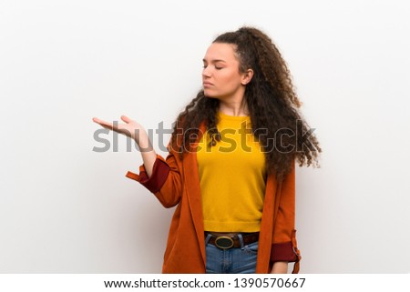 Teenager girl with coat holding copyspace with doubts