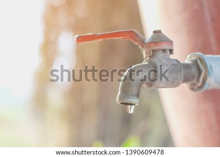 Water that is dripping from the old faucet that connects to the pvc pipe with red jar and blurred backgrounds and orange light in the outdoors.