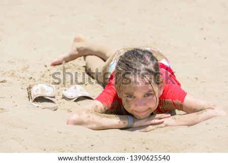 Dirty girl in the sand is lying on beach in red tshirt in hot sun
