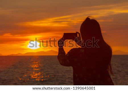 The silhouette of a girl shooting a sunset at the beach.