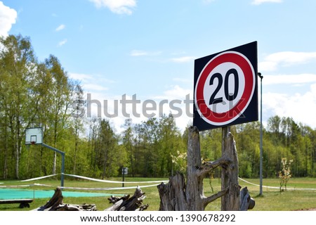 Maximum speed limit traffic sign number 20 in red circle on green landscape and blue sky background with copy space.
