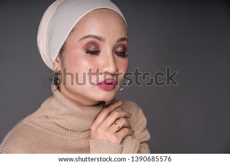 Close up portrait of a beautiful Muslim female model wearing sweatshirt with hijab sitting on a chair isolated over grey background. Studio fashion and beauty concept.