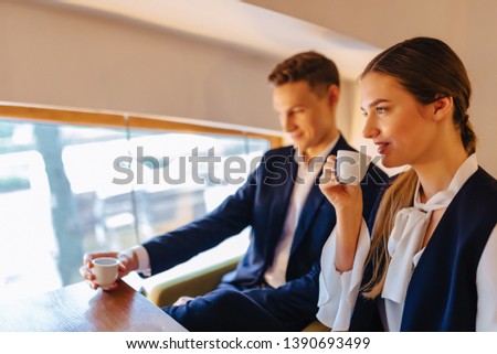 A stylish couple drinks morning coffee at the cafe with cozy interior, young businessmen and freelancers