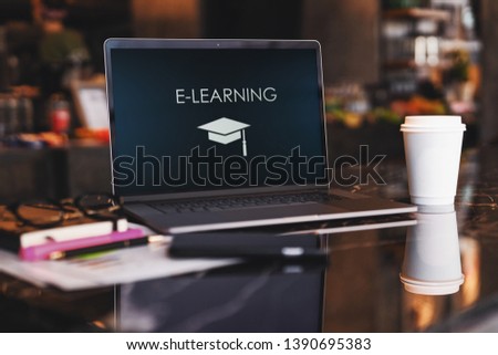 Close up of laptop with inscription on screen e-learning and image of square academic cap on table in empty room, cafe. Workplace without people. Distance learning. Online education, e-learning.