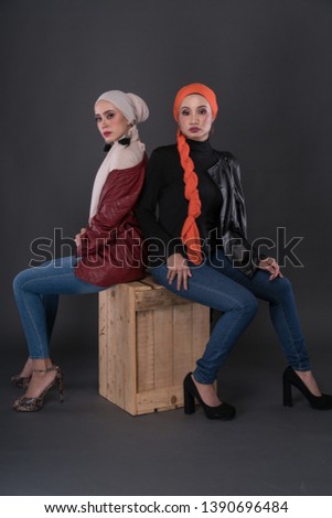 Fashionable female models in jeans, long sleeves leather jacket, high heels and hijab isolated on grey background. Stylish Muslim female hijab fashion lifestyle portraiture concept.