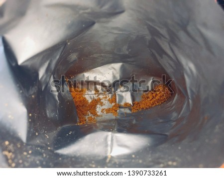 Close up of cheese powder and small pieces of corn snack left inside the bottom of reflective snack foil bag 