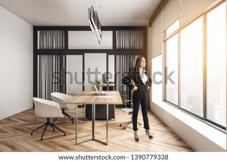 Attractive young european businesswoman standing in modern office interior with furniture, wooden floor, concrete walls and city view. Research and executive concept