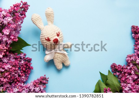 Lilac flowers with knitting toy rabbit on blue background. Top view, flat lay, copy space.