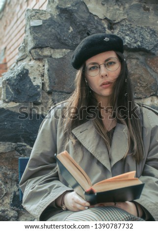 young beautiful woman in casual style clothes reading book outdoor. portrait of student. woman in glasses and black beret. typical nerd portrait. scene of city lifestyle