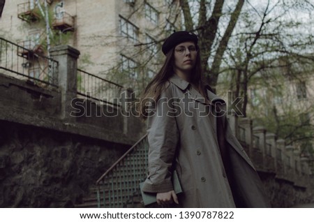 beautiful woman in grey trench coat and black beret on the street. outdoor scene of city lifestyle: casual clothes, grey colors, building on the background. portrait of city dweller