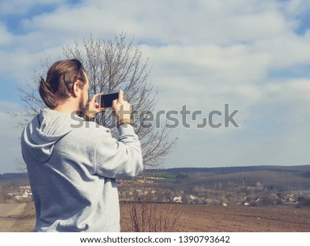 Young man walking in the wild nature and photographing landscape by mobile phone .