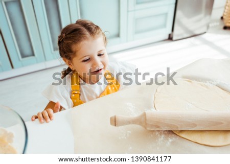 excited child looking at dough with wooden rolling pin on baking parchment paper
