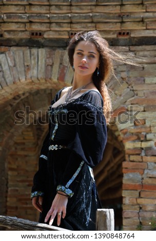 Attractive young woman in a medieval dress standing in the inner courtyard of the ancient castle
