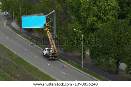 Empty blue billboard being installed by workers on crane 