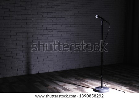 Microphone on dark stage near brick wall. Space for text