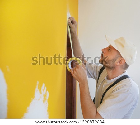 Man putting tape on the wall. The simple step for the quick and easy painting process. Renovation house concept.