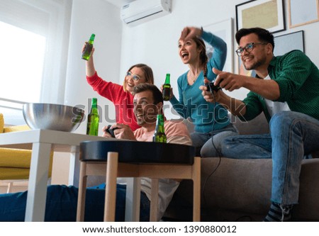 Group of friends sitting on sofa in living room and playing video games at home.