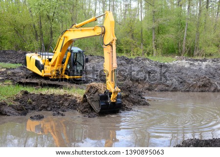 Big powerful excavator digging drainage channel in swamp in countryside