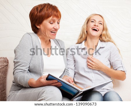 Mother and daughter looking photo book. Two laughing smiling women at home