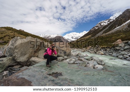 Young female tourist in softshell jacket taking photos of the amazing scenery of the Hooker Lake ath the Hooker Valley of Aoraki/Mount Cook National Park, South Island, New Zealand.