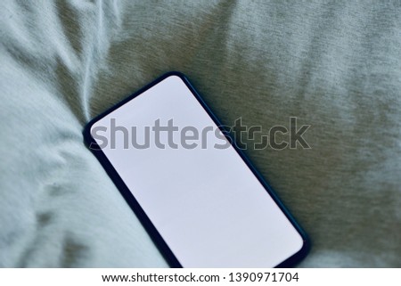 Edge to edge full screen smartphone with copy space on green bed sheet, cozy feeling.