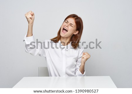 Cute business woman in a white shirt gesticulates with her hands while sitting at the office desk office gray background