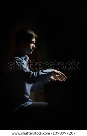 young man sitting at the piano. boy emotionally plays the keyboard instrument in the music school. student learns to play. hands pianist. black dark background. vertical.