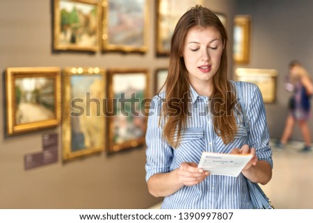 Portrait of young woman with a guide looking at pictures at museum of arts