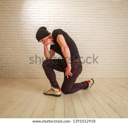 Young guy in casual style hip-hop and breakdance dancer pose in the studio on a background of a brick wall