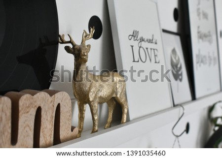 miniature statue of deer in focus on white wooden shelf with isolated pictures behind