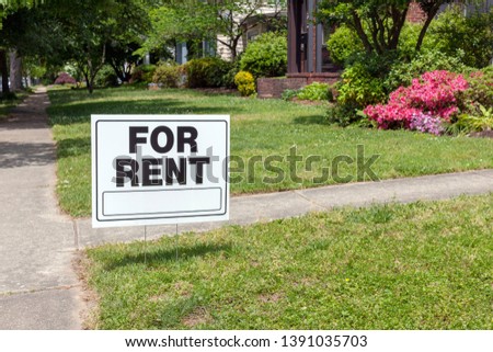 FOR RENT sign posted in lawn advertising home for rent.