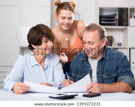 Adult couple is singing contract with their daughter indoor.