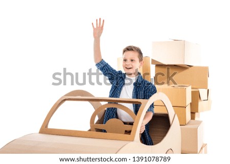 adorable smiling boy sitting in cardboard car and waving Isolated On White