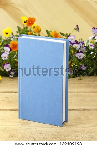 Blue book isolated on wooden background. Fresh blooming flowers in the background.
