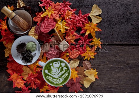 Creative flat lay photo of workspace desk, Autumn leaves matcha green tea cup wooden background, Place for text, dark photography